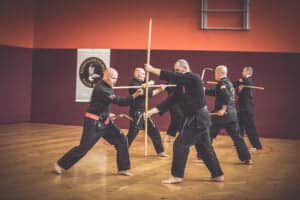 a group of men in black karate uniform training kobudo with Kama and Bo